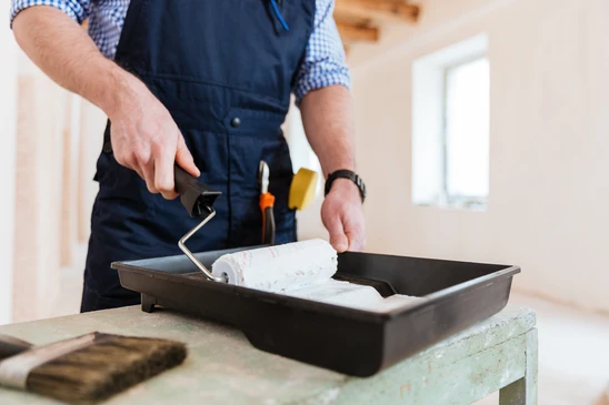 Un artisan peintre en salopette bleue pr&eacute;pare son mat&eacute;riel dans un int&eacute;rieur r&eacute;sidentiel