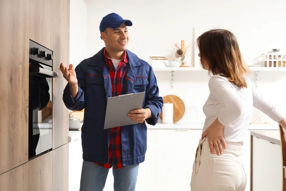 Artisan en salopette grise et t-shirt bleu consulte une notice technique assis au sol dans une pièce en rénovation